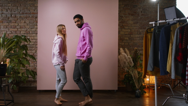 A fashion studio shooting of a happy young couple in hoodie posing over pink background.