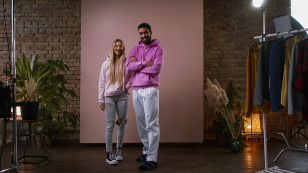 A fashion studio shooting of a happy young couple in hoodie posing over pink background.