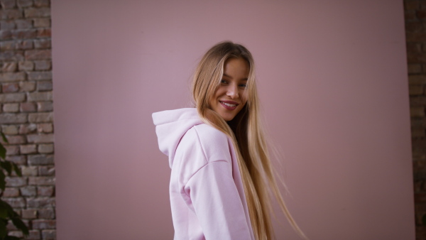 A fashion studio shooting of a happy young blonde woman in hoodie posing over pink background.