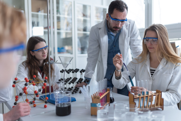 Science students with a teacher doing chemical reaction experiment in the laboratory at university.