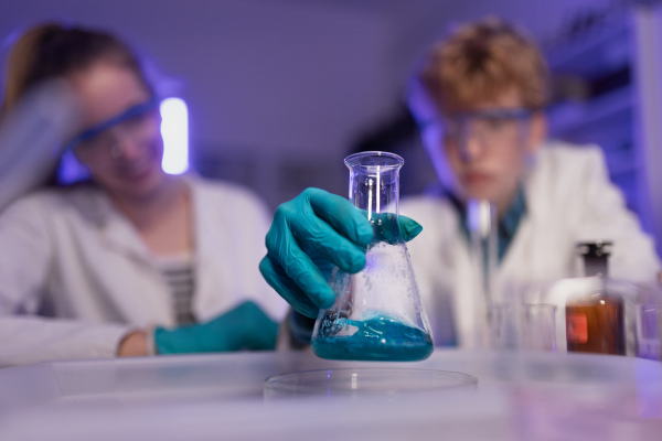 Science students doing chemical experiment in laboratory at university, close-up.