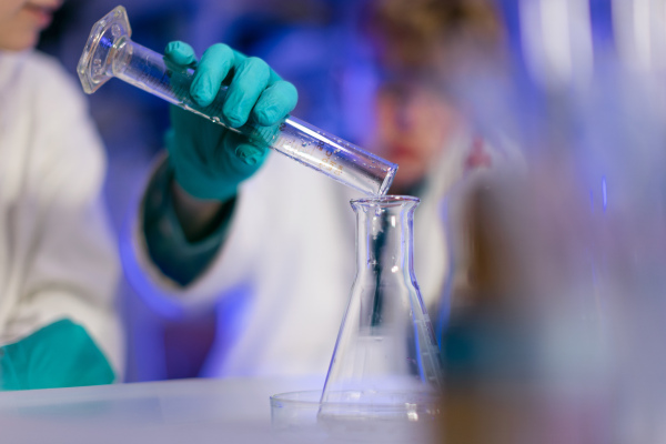 Science students doing chemical experiment in laboratory at university, close-up.