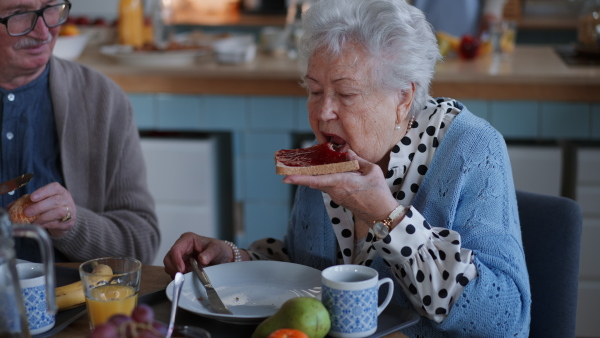 A smiling elderly woman and man enjoying breakfast in nursing home care center.