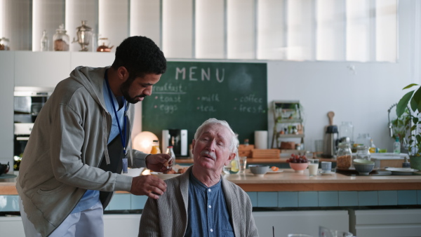 A caregiver helping senior man to insert hearing aid in his ear.