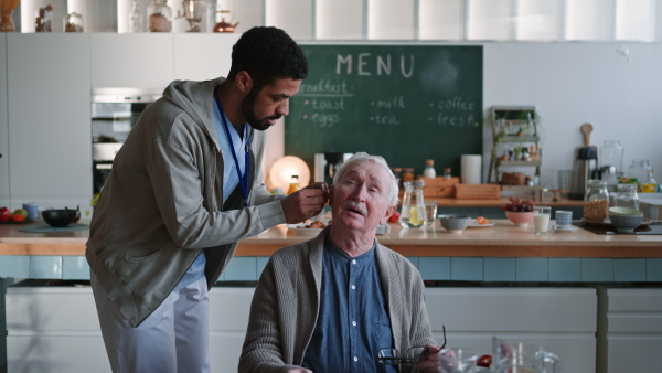 A caregiver helping senior man to insert hearing aid in his ear.