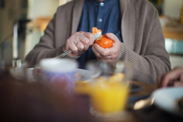 A close-up of senior man enjoying breakfast, peeling off apple in nursing home care center.