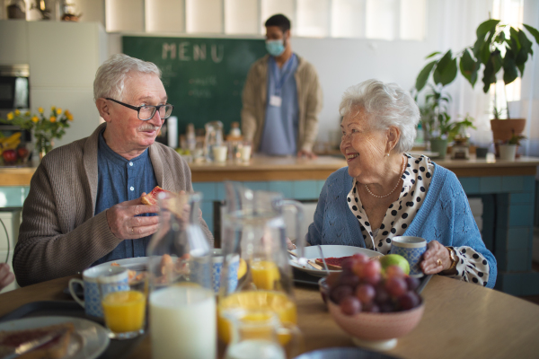 A smiling elderly woman and man enjoying breakfast in nursing home care center.