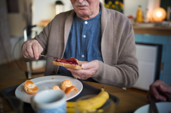 A close-up of senior man enjoying breakfast, spreading on bread in nursing home care center.