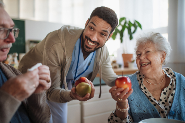 A caregiver bringing healthy snack to senior woman and man in nursing home care center.