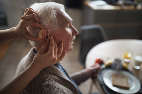 A caregiver helping senior man to insert hearing aid in his ear.