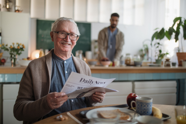 A smiling elderly man enjoying breakfast and reading newspaper in nursing home care center.