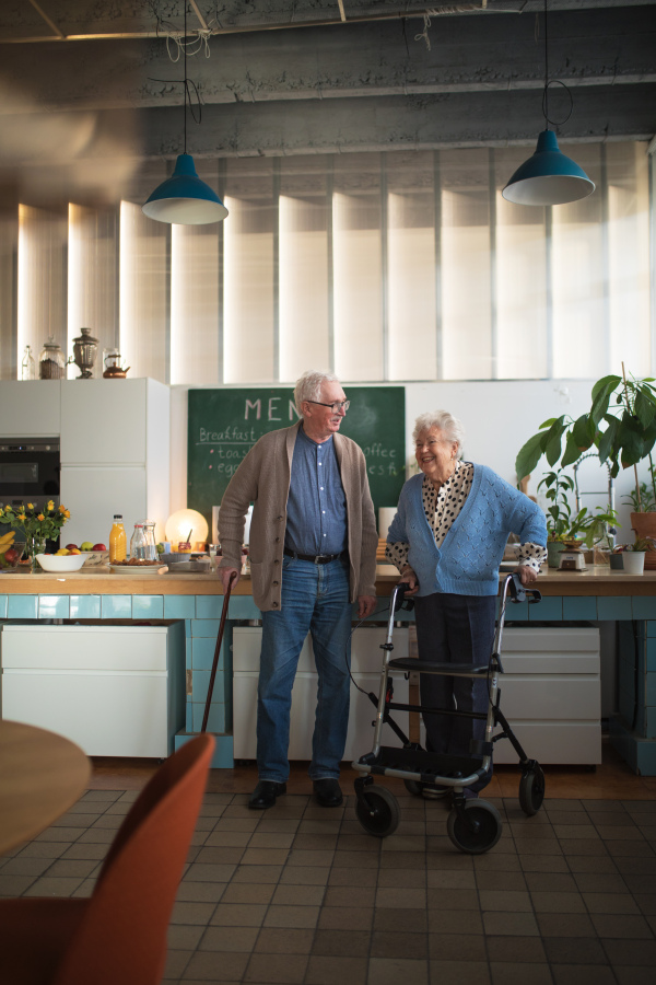 A senior man and woman walking with walker indoors in retirement nursing hme.