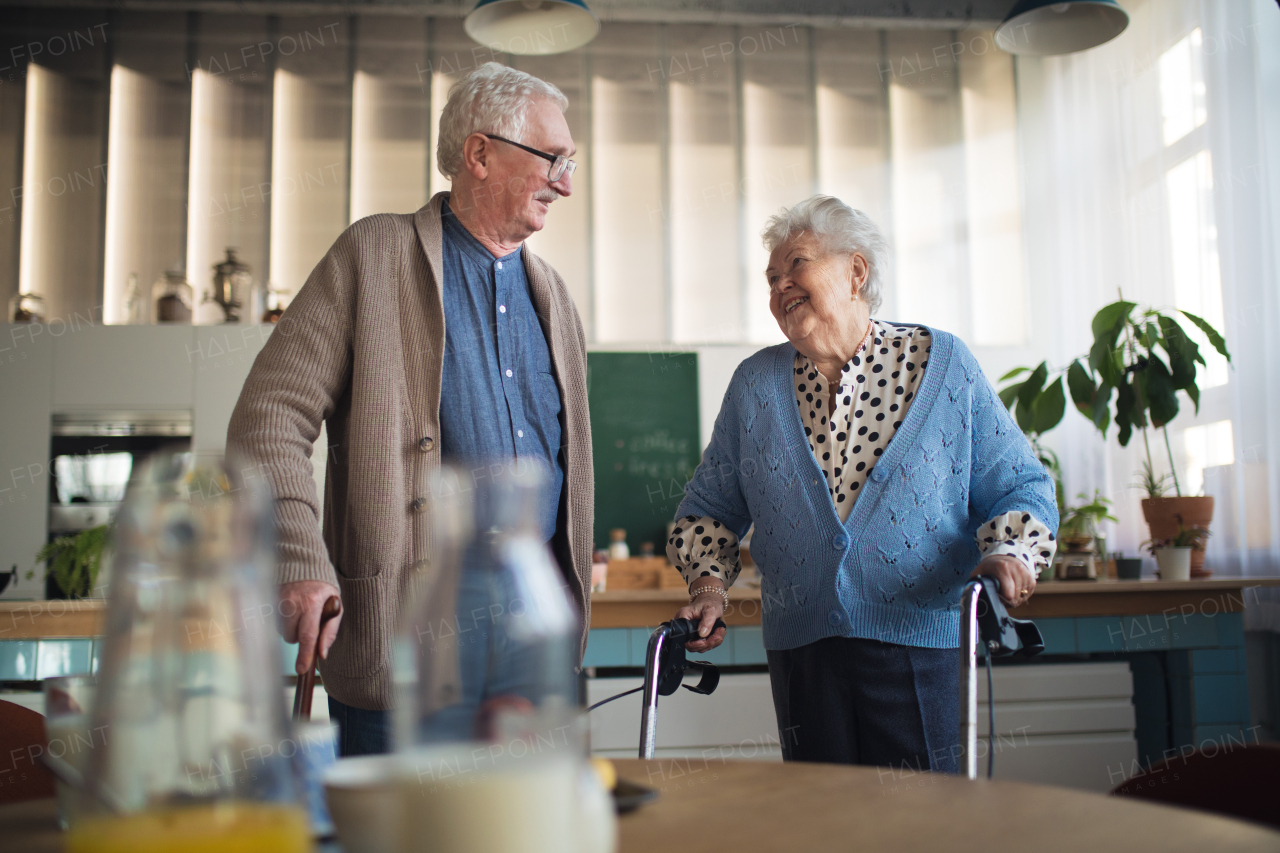 A senior man and woman walking with walker indoors in retirement nursing hme.