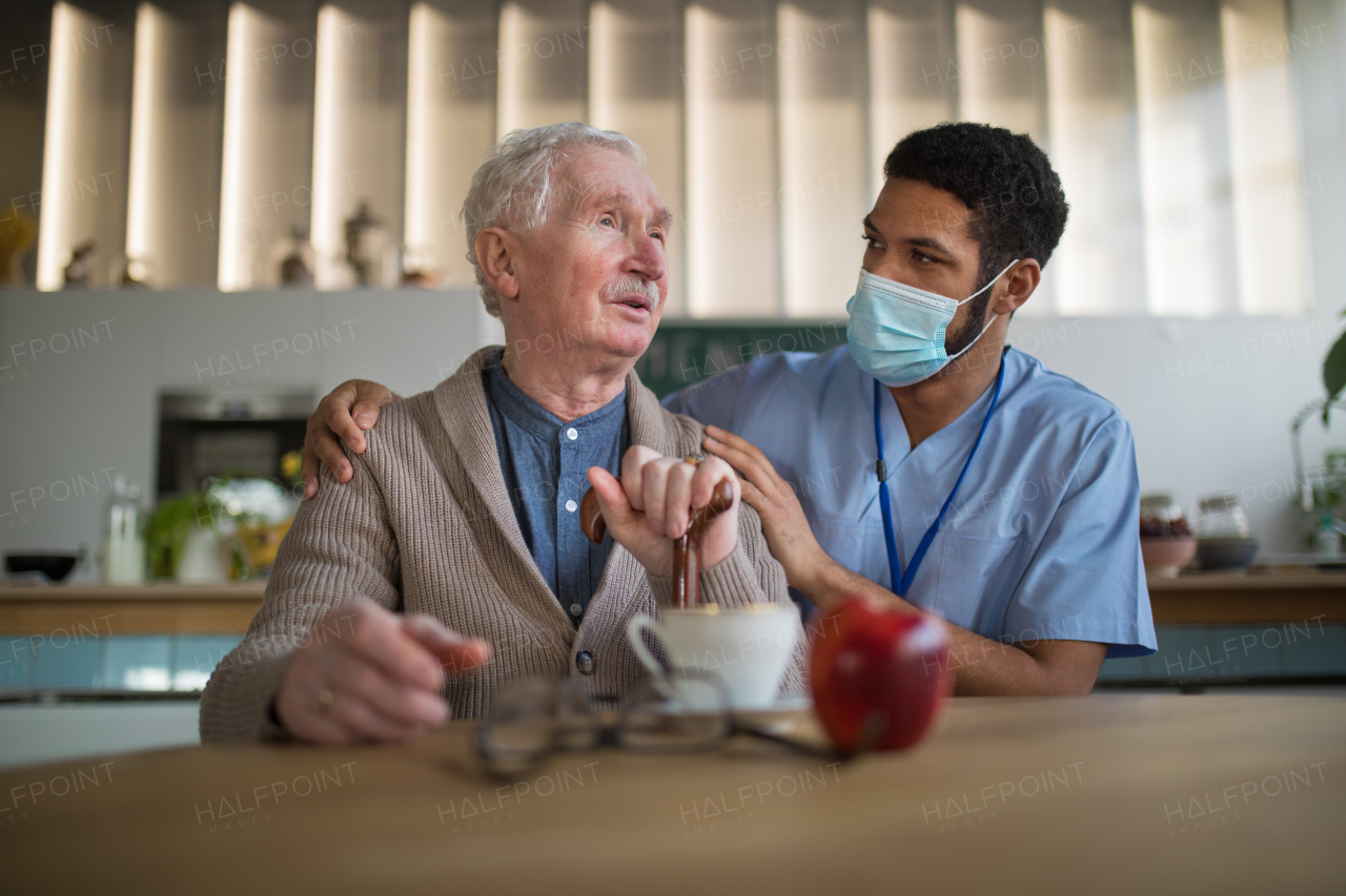 Caregiver with a medical mask bringing healthy snack to senior man in nursing home care center.