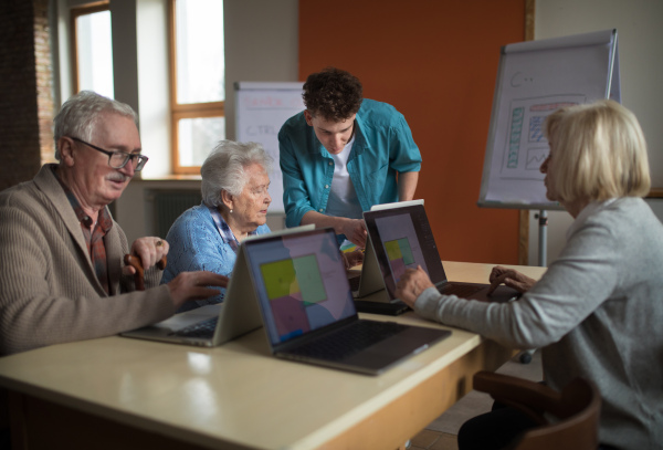 A senior group in retirement home with young instructor learning together in computer class