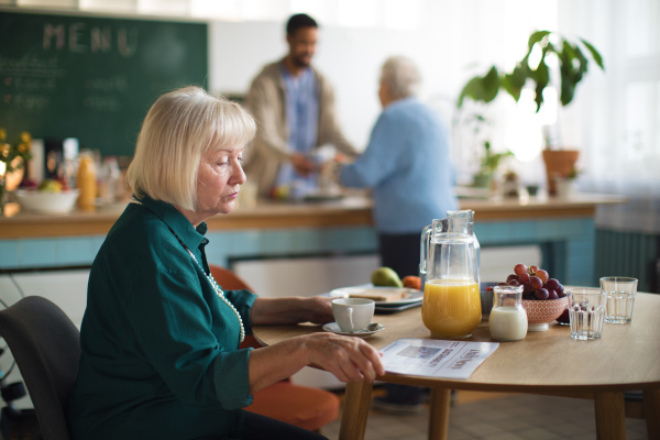 An elderly woman enjoying breakfast and reading newspaper in nursing home care center.