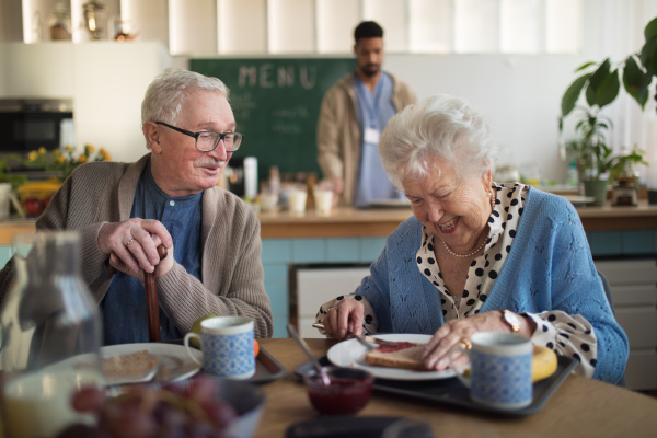 A smiling elderly woman and man enjoying breakfast in nursing home care center.