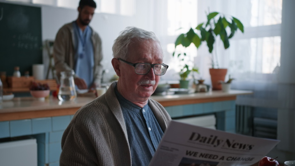 A smiling elderly man enjoying breakfast and reading newspaper in nursing home care center.