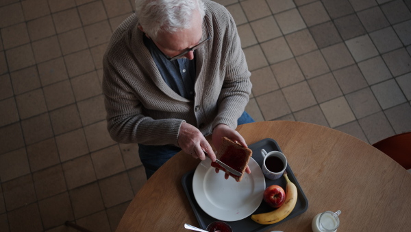 A high angle view of senior man enjoying breakfast in nursing home care center.