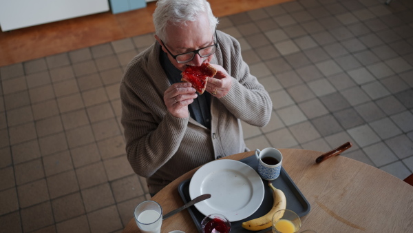 A high angle view of senior man enjoying breakfast in nursing home care center.