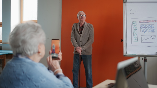 A senior woman taking a picture of her friend during computer class.