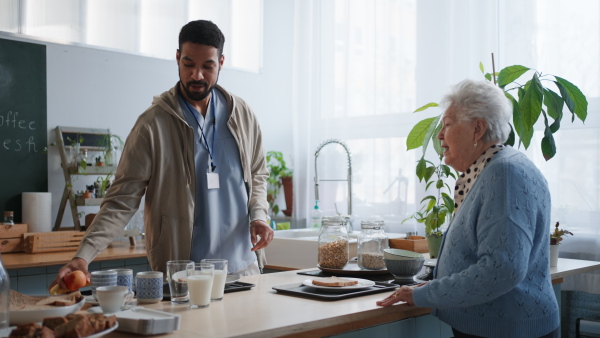 A young caregiver serving breakfast to elderly woman in nursing home care center.