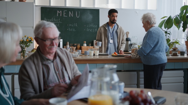 A young caregiver serving breakfast to elderly woman in nursing home care center.