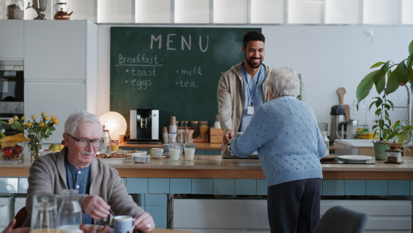 A young caregiver serving breakfast to elderly woman in nursing home care center.