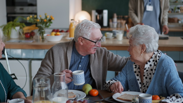 A smiling elderly woman and man enjoying breakfast in nursing home care center.