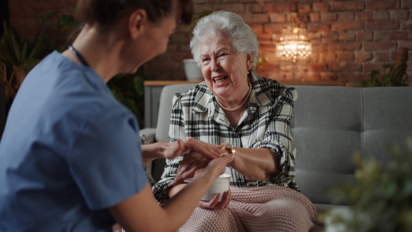 Nurse giving hand massage with cream to happy senior woman in retirement home, chatting