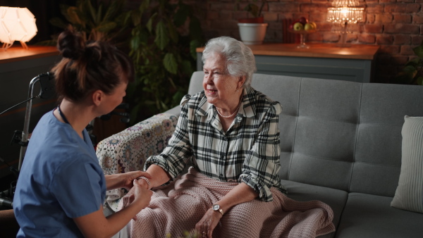 A female healthcare worker or caregiver visiting senior woman indoors at home, doing body care to patient.