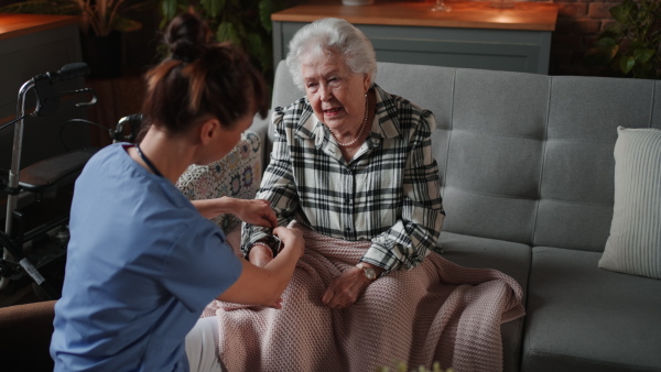 A female healthcare worker or caregiver visiting senior woman indoors at home, doing body care to patient.