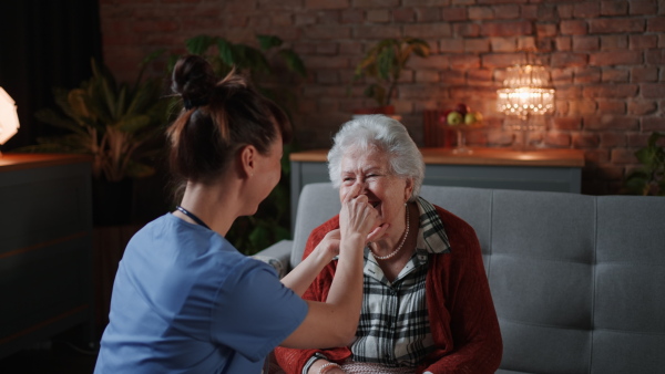 A female healthcare worker or caregiver visiting senior woman indoors at home, doing body care to patient.