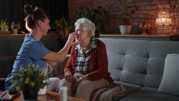 A female healthcare worker or caregiver visiting senior woman indoors at home, doing body care to patient.