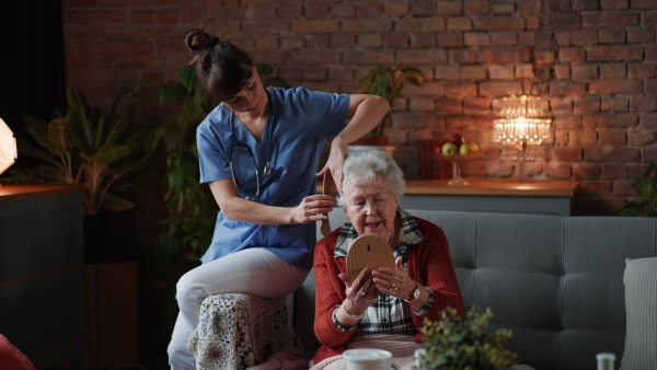 Nurse combing hair of senior woman observing herself in a mirror in retirement home