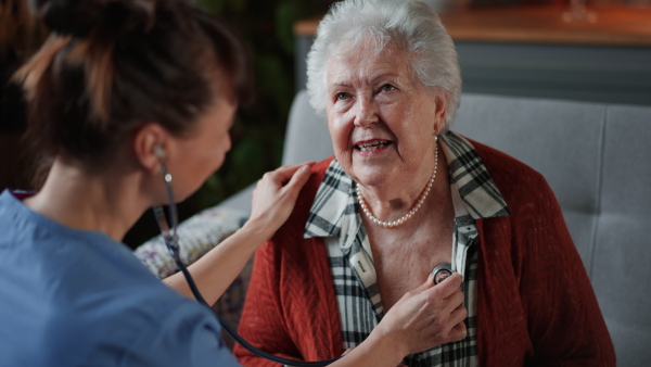 A female doctor doing check up to senior woman indoors at home during home visit