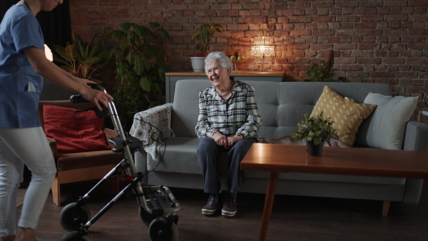 A female healthcare worker or caregiver visiting senior woman indoors at home, helping to walk.