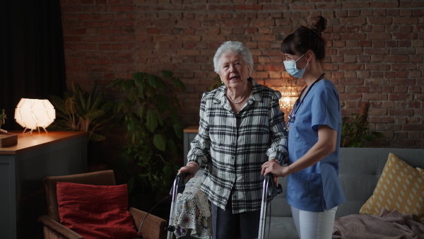 Senior woman with medical nurse in retirement home, standing with crutches, talking, smiling