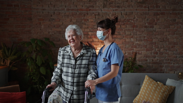 A female healthcare worker or caregiver visiting senior woman indoors at home, helping to walk.