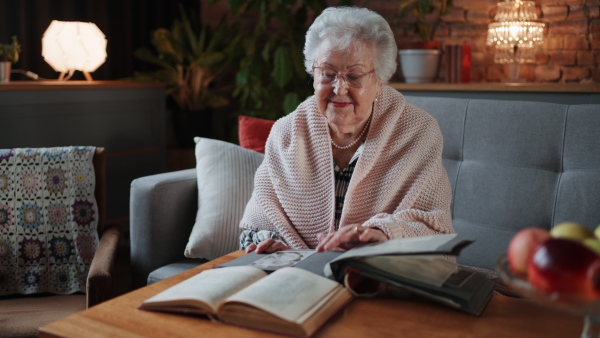 A happy senior woman sitting on sofa at home and looking at old photos.