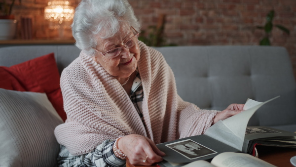 Elderly woman looking at photographs in album at home, covered by a blanket