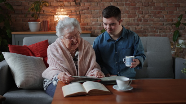 A grandmother showing old photos to her grandson with Down syndrome at home.