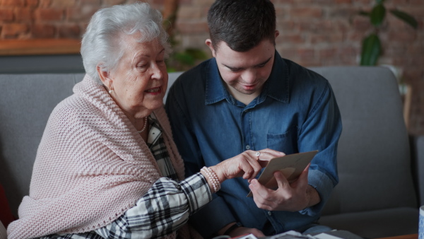 A grandmother showing old photos to her grandson with Down syndrome at home.