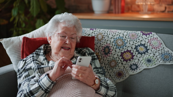 Senior woman resting on sofa, looking at her smart phone, smiling