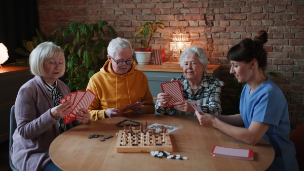 Seniors playing board game in their retirement home, nurse is playing with them.