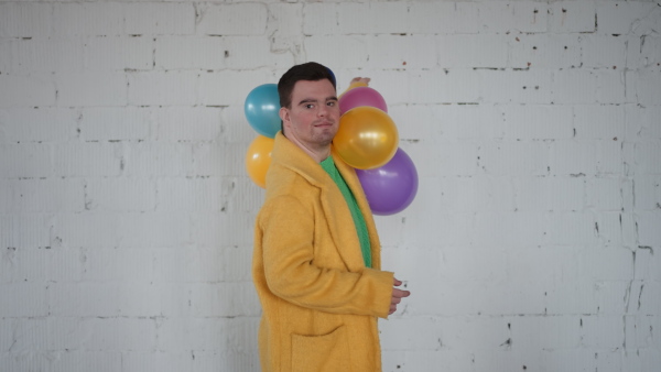 Happy boy with down syndrome posing with a colourful baloons in front of white wall, during his birthday party.