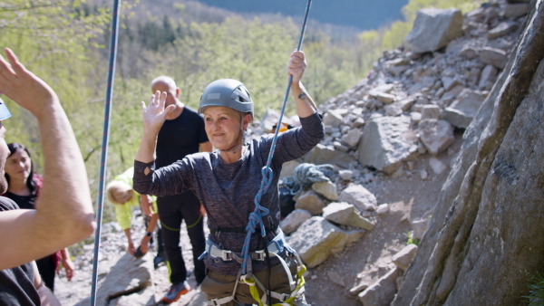 A group of seniors with instructor celebrating successful rocks climbing outdoors in nature, active lifestyle.