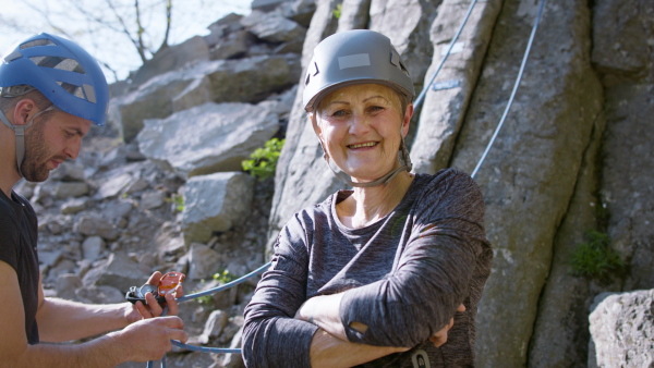 A senior man with instructor getting ready for rocks climbing outdoors in nature, active lifestyle.