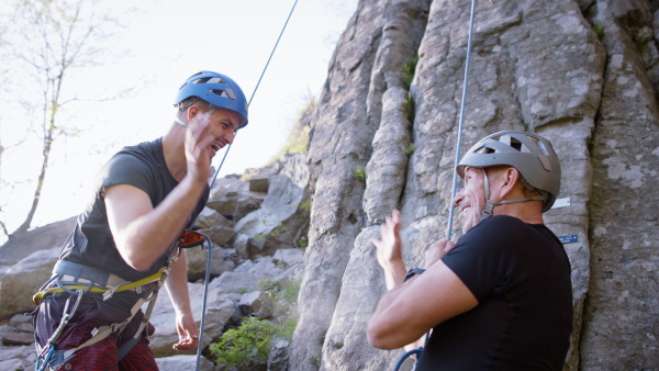 A senior man with instructor getting ready for rocks climbing outdoors in nature, active lifestyle. Instructor wishing good luck.