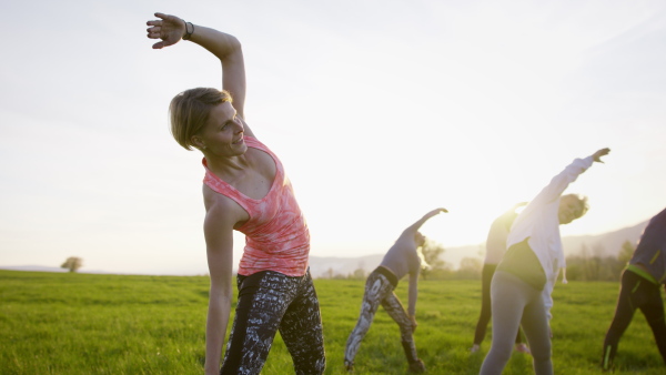 A group of seniors with sport instructor doing exercise outdoors in nature, active lifestyle.